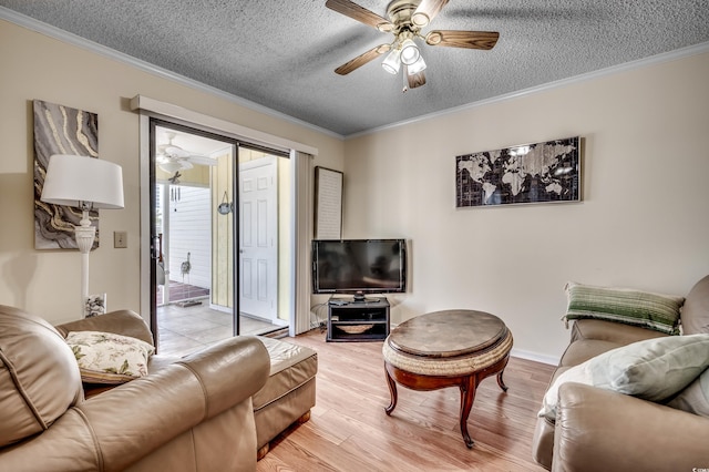 living room featuring ceiling fan, ornamental molding, a textured ceiling, and light wood-type flooring