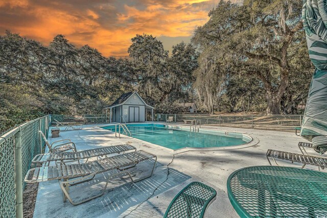 pool at dusk with a patio and a storage shed