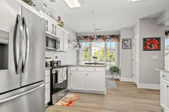 kitchen featuring stainless steel appliances, hanging light fixtures, white cabinets, and light hardwood / wood-style flooring