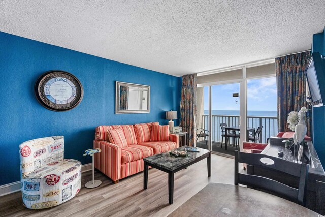 living room featuring floor to ceiling windows, a textured ceiling, a water view, and hardwood / wood-style floors