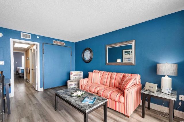 living area with visible vents, a textured ceiling, baseboards, and wood finished floors