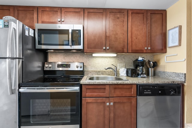 kitchen with brown cabinetry, decorative backsplash, appliances with stainless steel finishes, and a sink