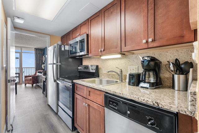 kitchen featuring light wood-type flooring, a sink, appliances with stainless steel finishes, brown cabinets, and backsplash