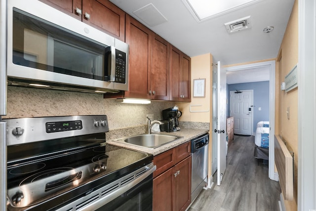 kitchen featuring light wood finished floors, visible vents, brown cabinets, stainless steel appliances, and a sink