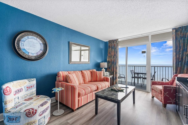 living room with a water view, a textured ceiling, wood finished floors, a wall of windows, and a textured wall