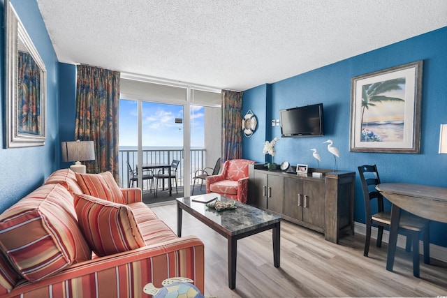 living area featuring expansive windows, a textured ceiling, light wood-style floors, baseboards, and a textured wall