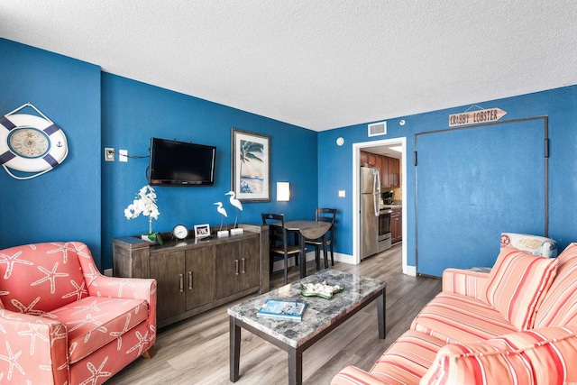 living room with baseboards, wood finished floors, visible vents, and a textured ceiling