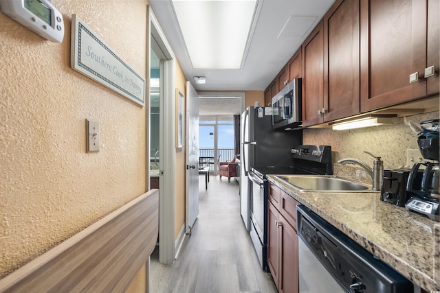 kitchen with light wood-style flooring, a sink, appliances with stainless steel finishes, decorative backsplash, and a textured wall