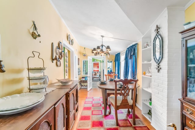 dining space with ornamental molding, light wood-type flooring, lofted ceiling, and a notable chandelier