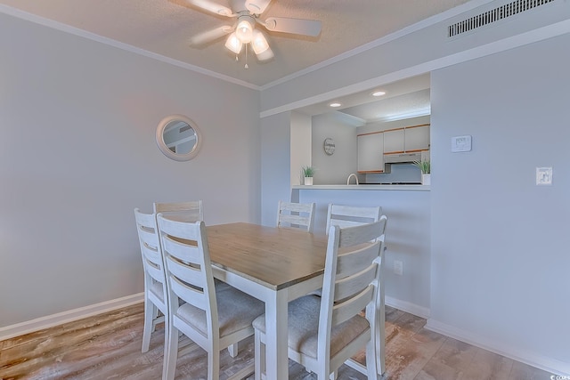 dining area with baseboards, light wood-style flooring, visible vents, and crown molding