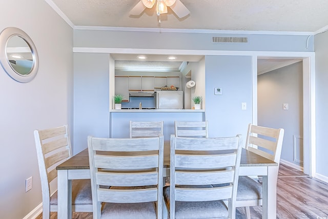 dining room featuring ceiling fan, visible vents, crown molding, and wood finished floors