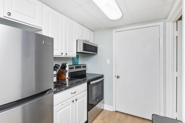 kitchen featuring white cabinetry, light hardwood / wood-style flooring, dark stone counters, stainless steel appliances, and a drop ceiling