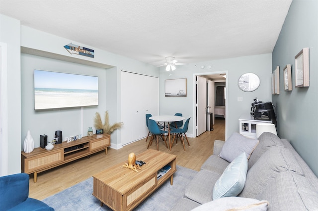 living room featuring ceiling fan, light hardwood / wood-style floors, and a textured ceiling