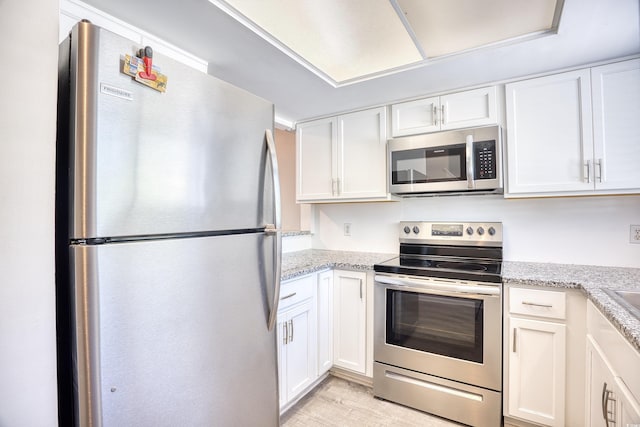 kitchen featuring light stone counters, white cabinetry, stainless steel appliances, and light wood-type flooring