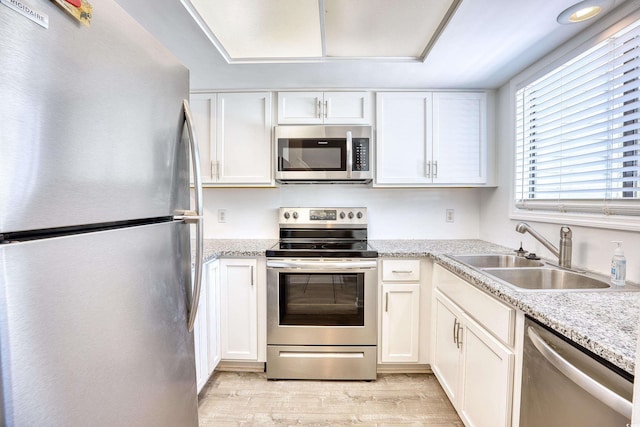 kitchen with light stone countertops, stainless steel appliances, sink, light hardwood / wood-style flooring, and white cabinetry