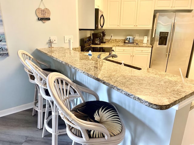 kitchen featuring white cabinets, kitchen peninsula, a breakfast bar area, and black appliances