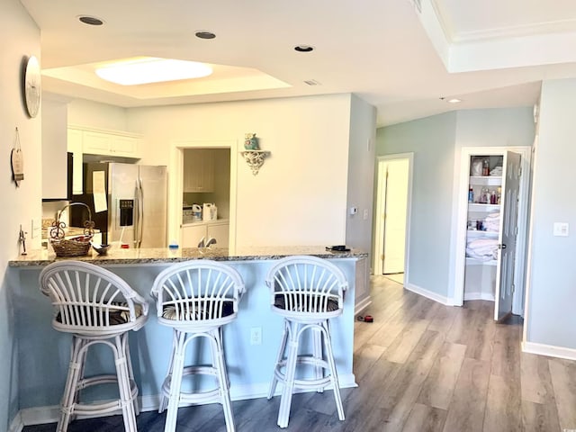 kitchen featuring kitchen peninsula, a raised ceiling, light hardwood / wood-style flooring, stainless steel fridge with ice dispenser, and white cabinetry