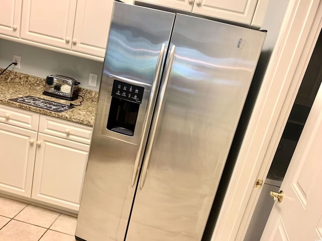 kitchen with stainless steel refrigerator with ice dispenser, light tile patterned floors, white cabinetry, and light stone counters