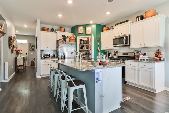 kitchen featuring stainless steel appliances, an island with sink, white cabinets, and light stone counters