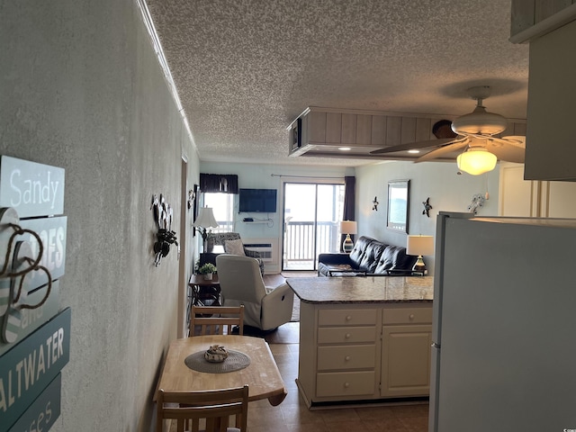 kitchen featuring kitchen peninsula, ceiling fan, refrigerator, and light stone counters