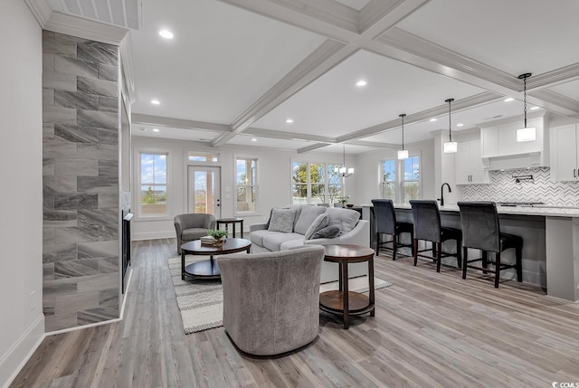 living room featuring coffered ceiling, sink, an inviting chandelier, beamed ceiling, and light hardwood / wood-style flooring