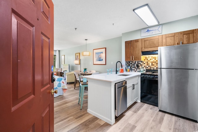 kitchen with kitchen peninsula, appliances with stainless steel finishes, light wood-type flooring, sink, and decorative light fixtures