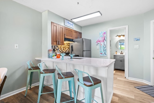 kitchen featuring a breakfast bar, backsplash, light hardwood / wood-style flooring, stainless steel fridge, and kitchen peninsula