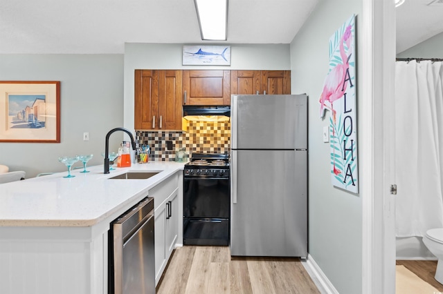 kitchen featuring backsplash, sink, light wood-type flooring, appliances with stainless steel finishes, and kitchen peninsula