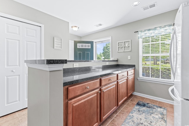 kitchen featuring white refrigerator, plenty of natural light, light tile patterned flooring, and kitchen peninsula