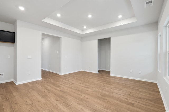 spare room with a raised ceiling and light hardwood / wood-style flooring