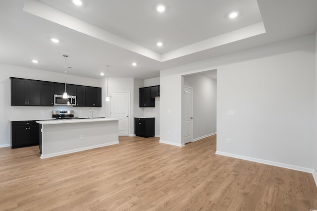 kitchen featuring a center island with sink, a raised ceiling, light wood-type flooring, and appliances with stainless steel finishes