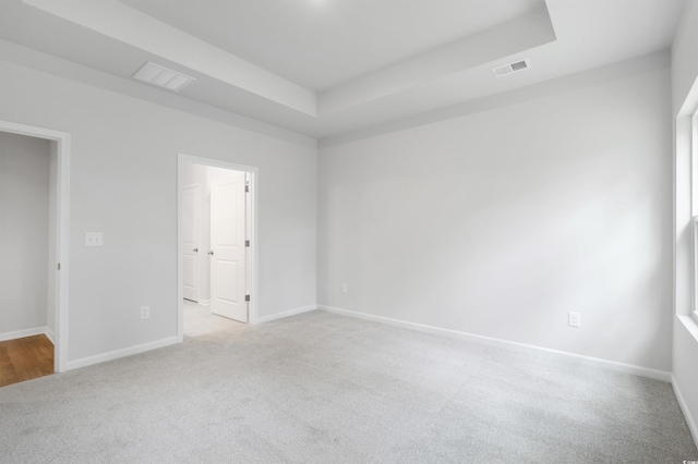 unfurnished room featuring light colored carpet and a tray ceiling