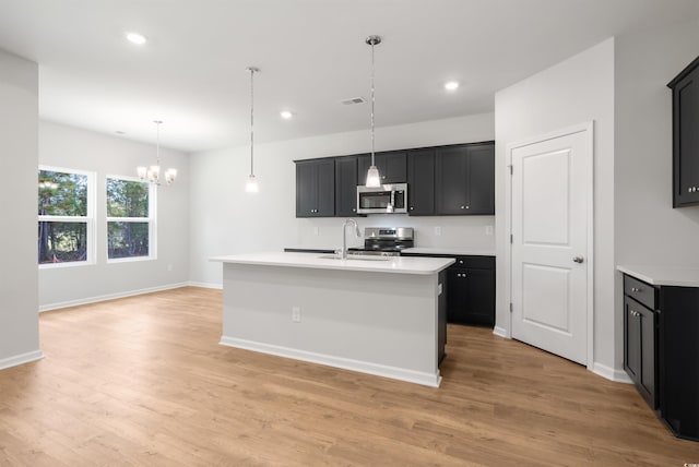 kitchen with sink, stainless steel appliances, an inviting chandelier, light hardwood / wood-style flooring, and an island with sink