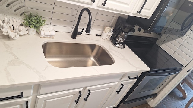 interior details featuring tasteful backsplash, white cabinetry, sink, and light stone countertops