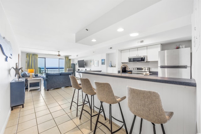 kitchen featuring a kitchen bar, stainless steel appliances, ceiling fan, light tile patterned floors, and white cabinetry