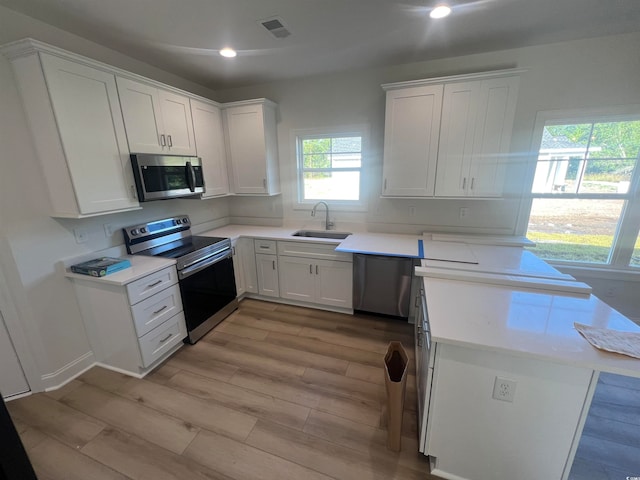 kitchen with stainless steel appliances, white cabinets, sink, and light hardwood / wood-style flooring