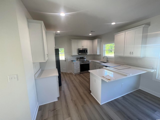 kitchen with stainless steel appliances, sink, kitchen peninsula, white cabinets, and light wood-type flooring