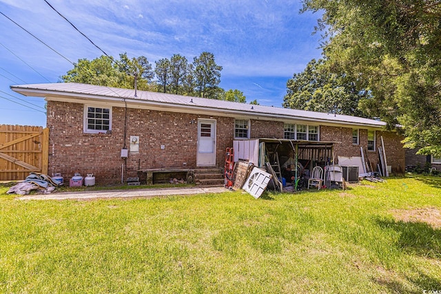 rear view of house with entry steps, a lawn, brick siding, and metal roof