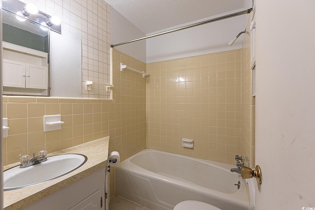 bathroom featuring toilet, a textured ceiling, tile walls, washtub / shower combination, and vanity