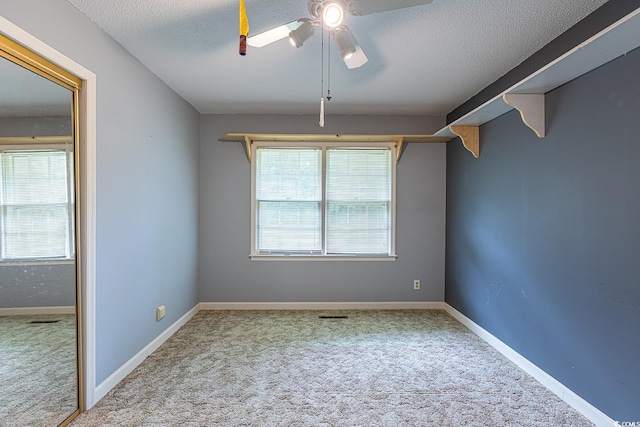 carpeted empty room with plenty of natural light, a textured ceiling, and a ceiling fan