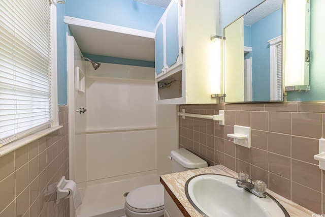 bathroom with tile walls, walk in shower, a wainscoted wall, toilet, and vanity