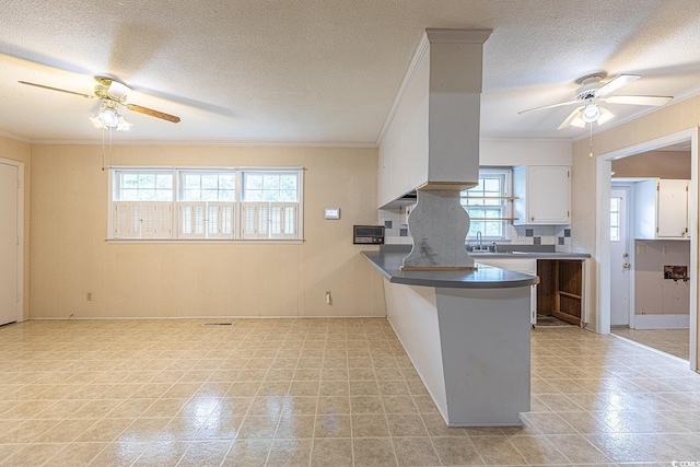 kitchen featuring white cabinetry, a peninsula, dark countertops, and a ceiling fan