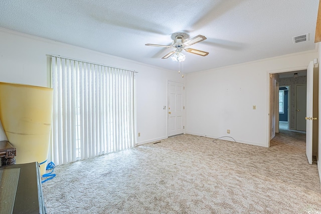 carpeted empty room featuring a healthy amount of sunlight, a ceiling fan, visible vents, ornamental molding, and a textured ceiling