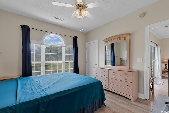 bedroom with light wood-type flooring, a ceiling fan, visible vents, and a textured ceiling