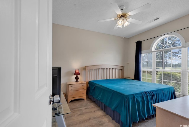 bedroom featuring visible vents, ceiling fan, light wood-style flooring, and a textured ceiling