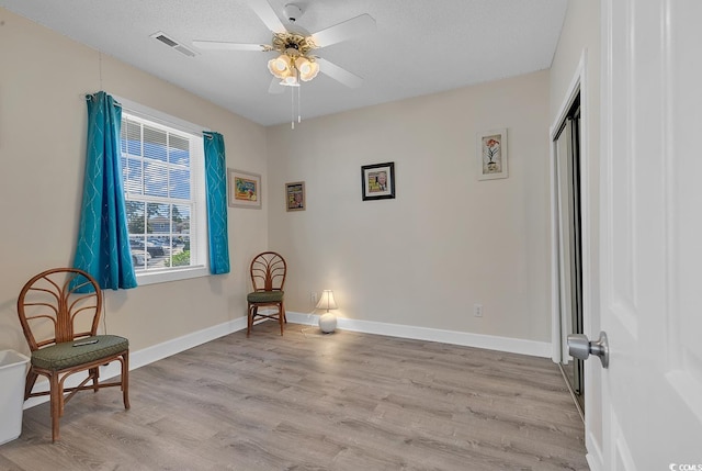 sitting room featuring light wood finished floors, baseboards, visible vents, and a textured ceiling