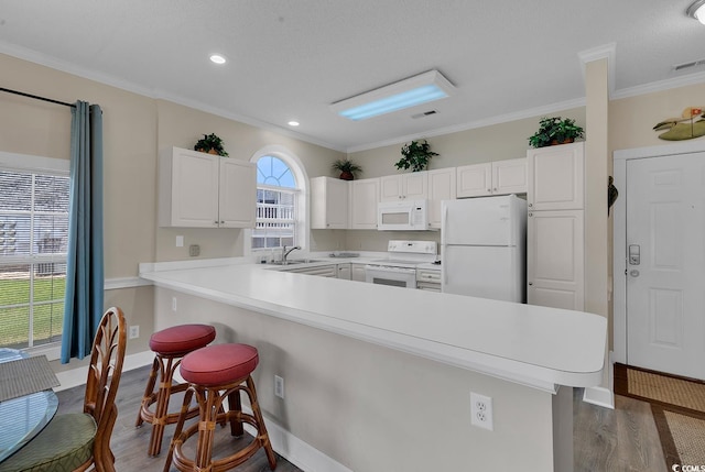 kitchen featuring white appliances, light countertops, a kitchen breakfast bar, and white cabinets