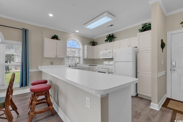 kitchen with white appliances, light wood finished floors, white cabinets, ornamental molding, and light countertops