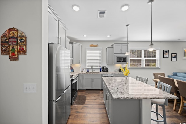 kitchen featuring a breakfast bar area, appliances with stainless steel finishes, dark hardwood / wood-style floors, decorative light fixtures, and a center island