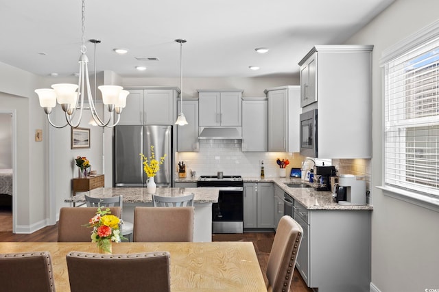 kitchen with hanging light fixtures, stainless steel appliances, sink, light stone countertops, and a center island